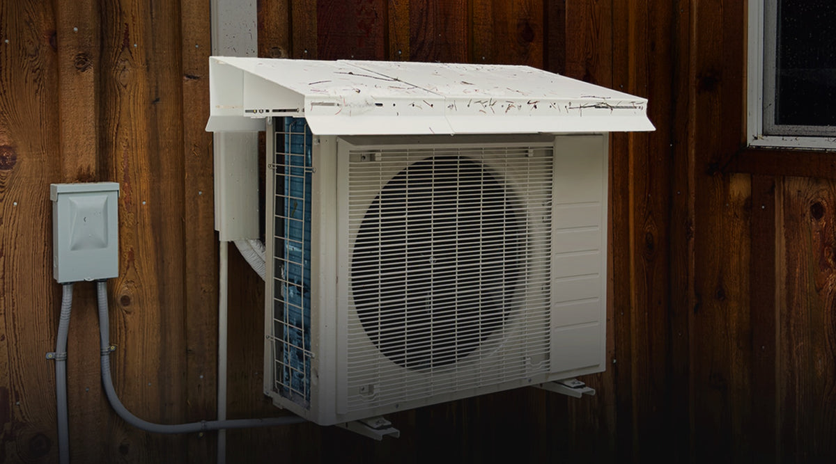 Heat Pump Snow Cap on a mini split heat pump against wood siding