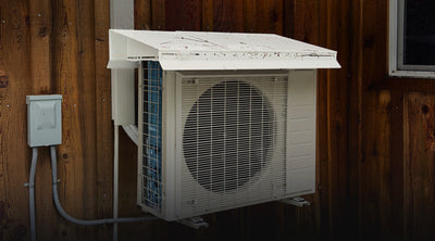 Heat Pump Snow Cap on a mini split heat pump against wood siding